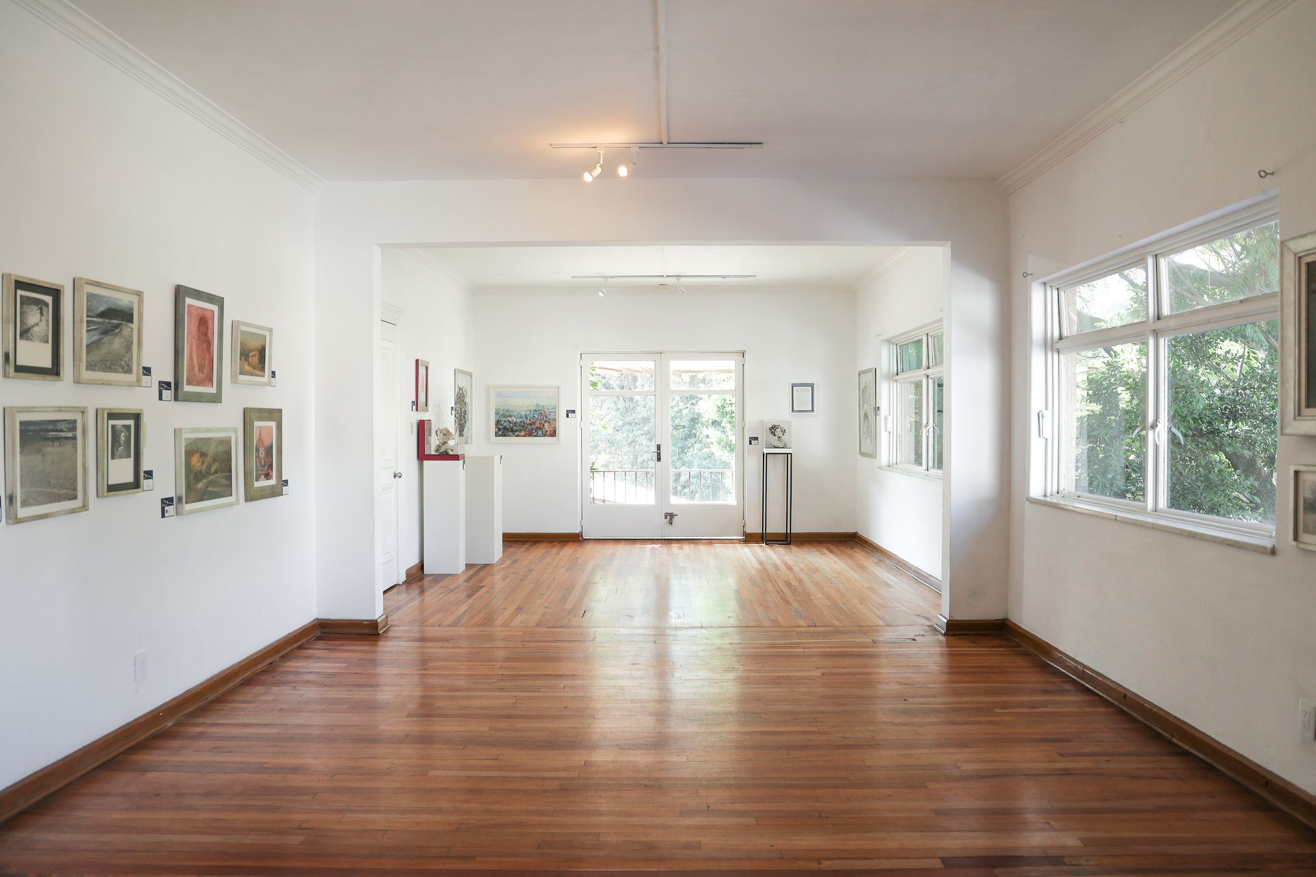 Galería de arte luminosa y vacía con paredes blancas, obras de arte enmarcadas y suelos de madera pulida.