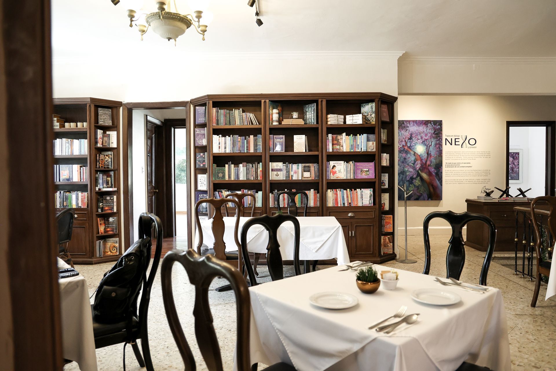 Elegante comedor con manteles blancos, sillas de madera oscura, estanterías y una iluminación cálida.