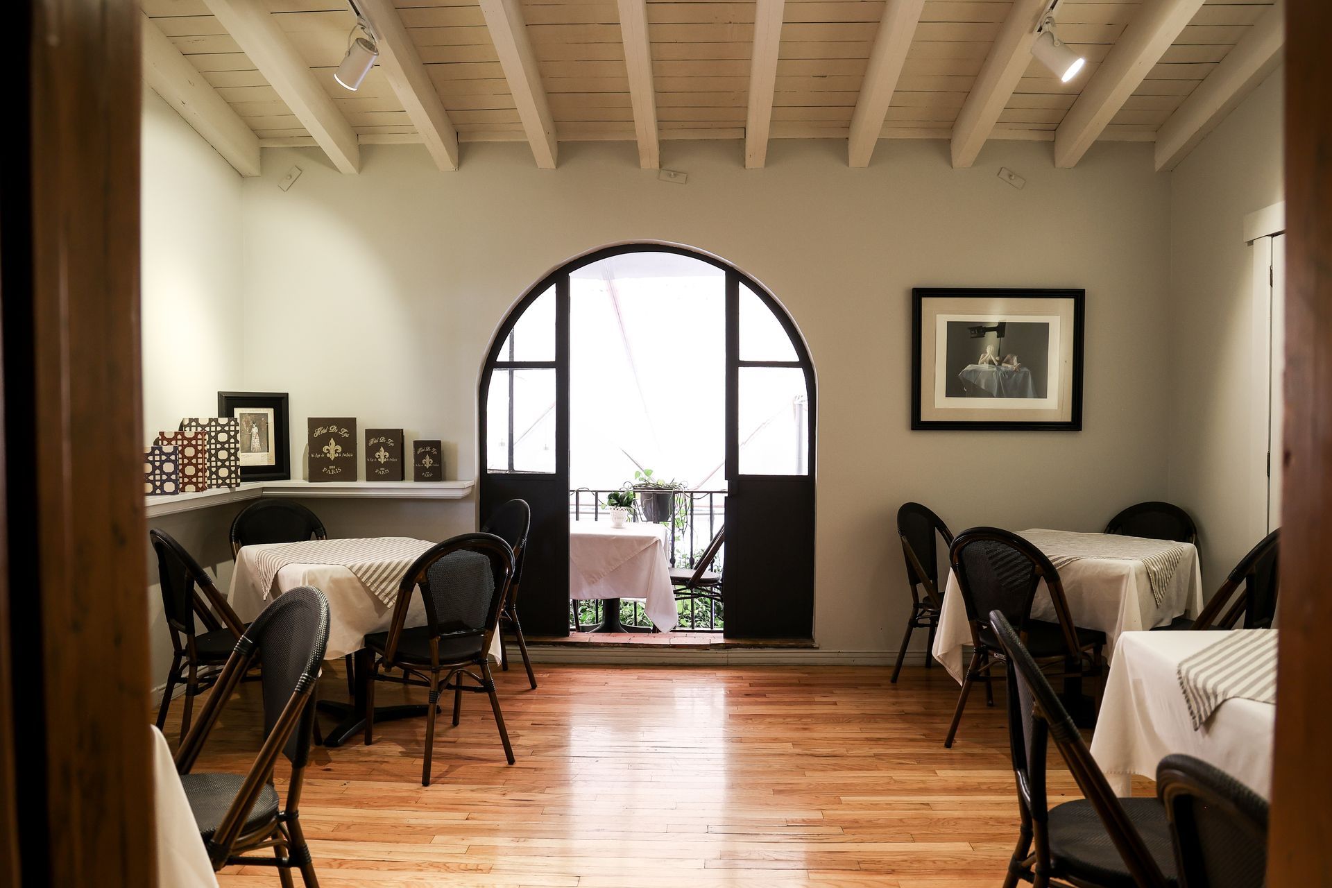 Elegante comedor con manteles blancos, puerta arqueada, suelo de madera y cuadros enmarcados en la pared.