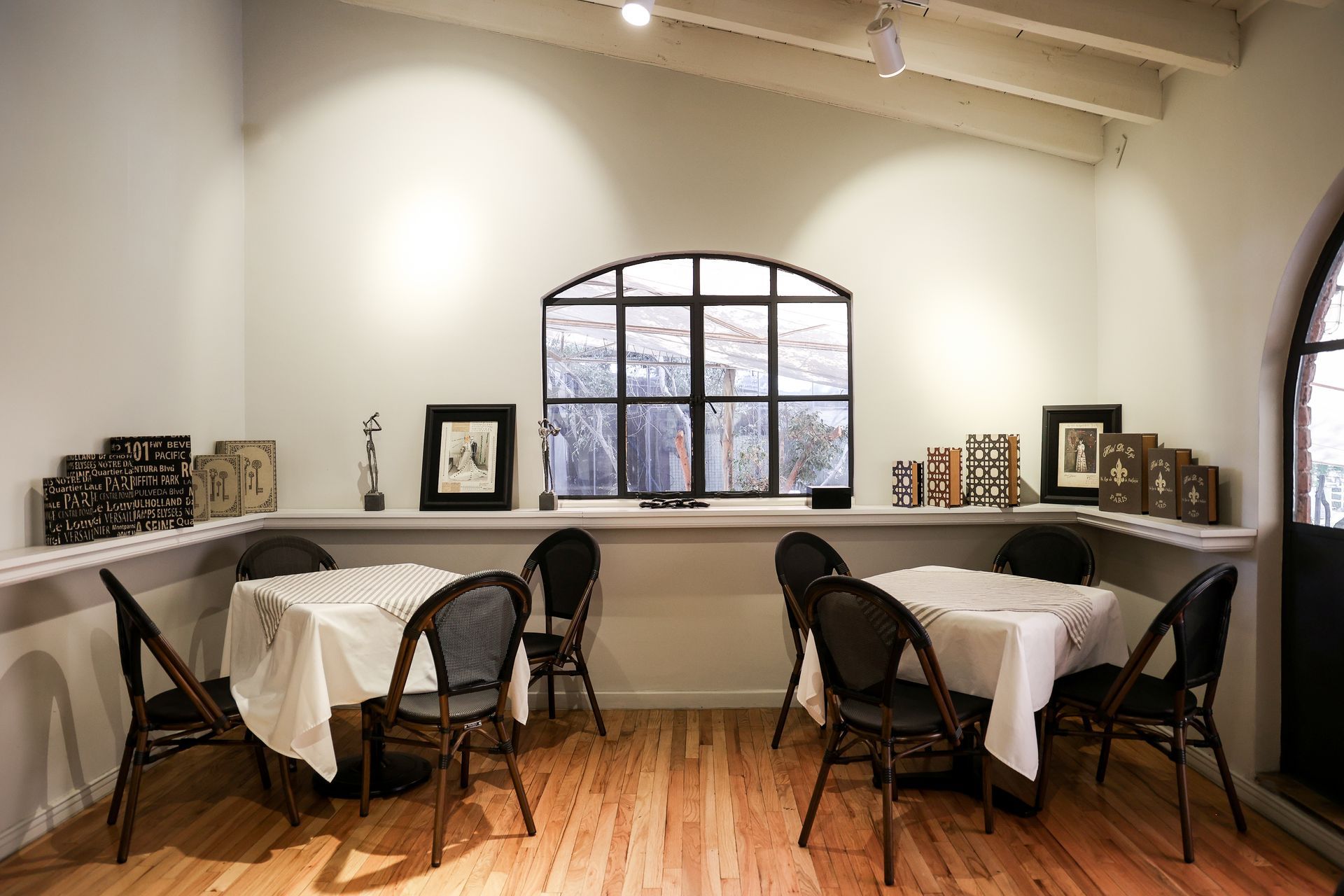 Comedor luminoso con ventanas arqueadas, mesas con manteles blancos y sillas negras sobre un suelo de madera.