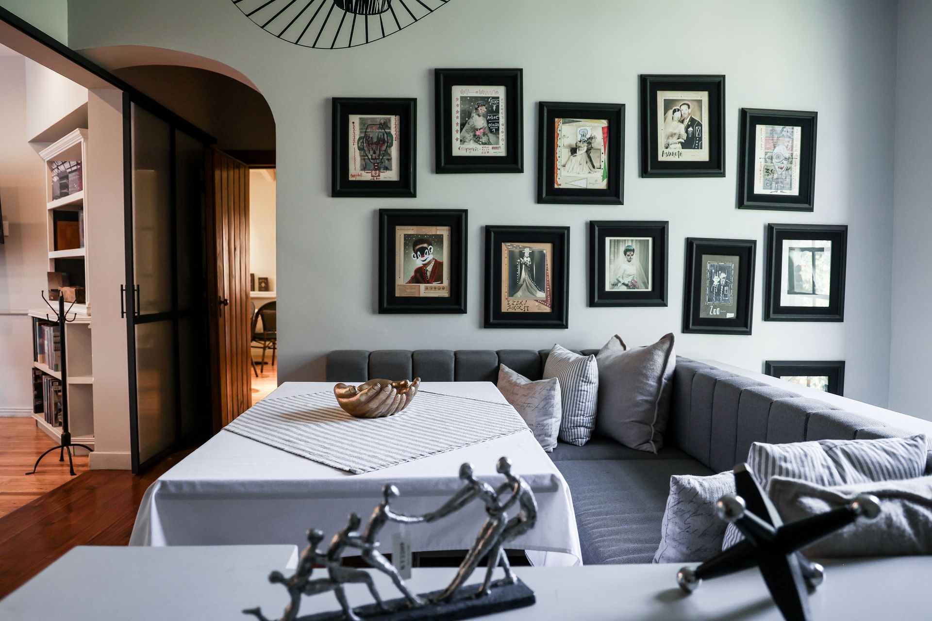 Sala de estar moderna con sofá gris, cuadro con marco negro y mesa de comedor junto a una puerta arqueada.