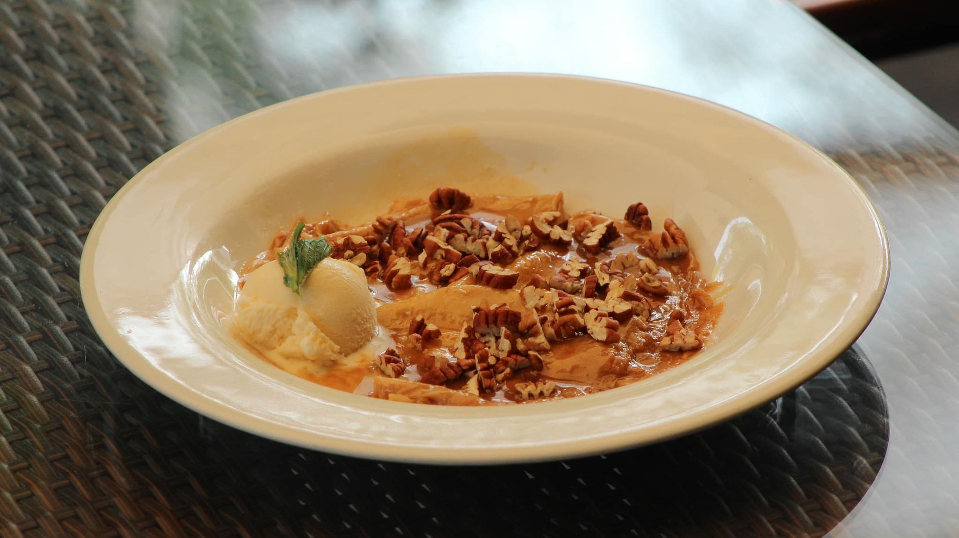 Postre cremoso en un tazón blanco, cubierto con nueces desmenuzadas y una guarnición de menta sobre una mesa.