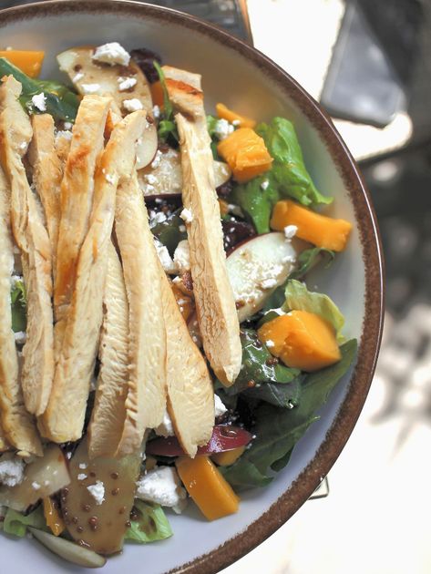 Tiras de pollo a la parrilla en un tazón de ensalada con hojas verdes, vegetales de color naranja y aderezo de arroz.
