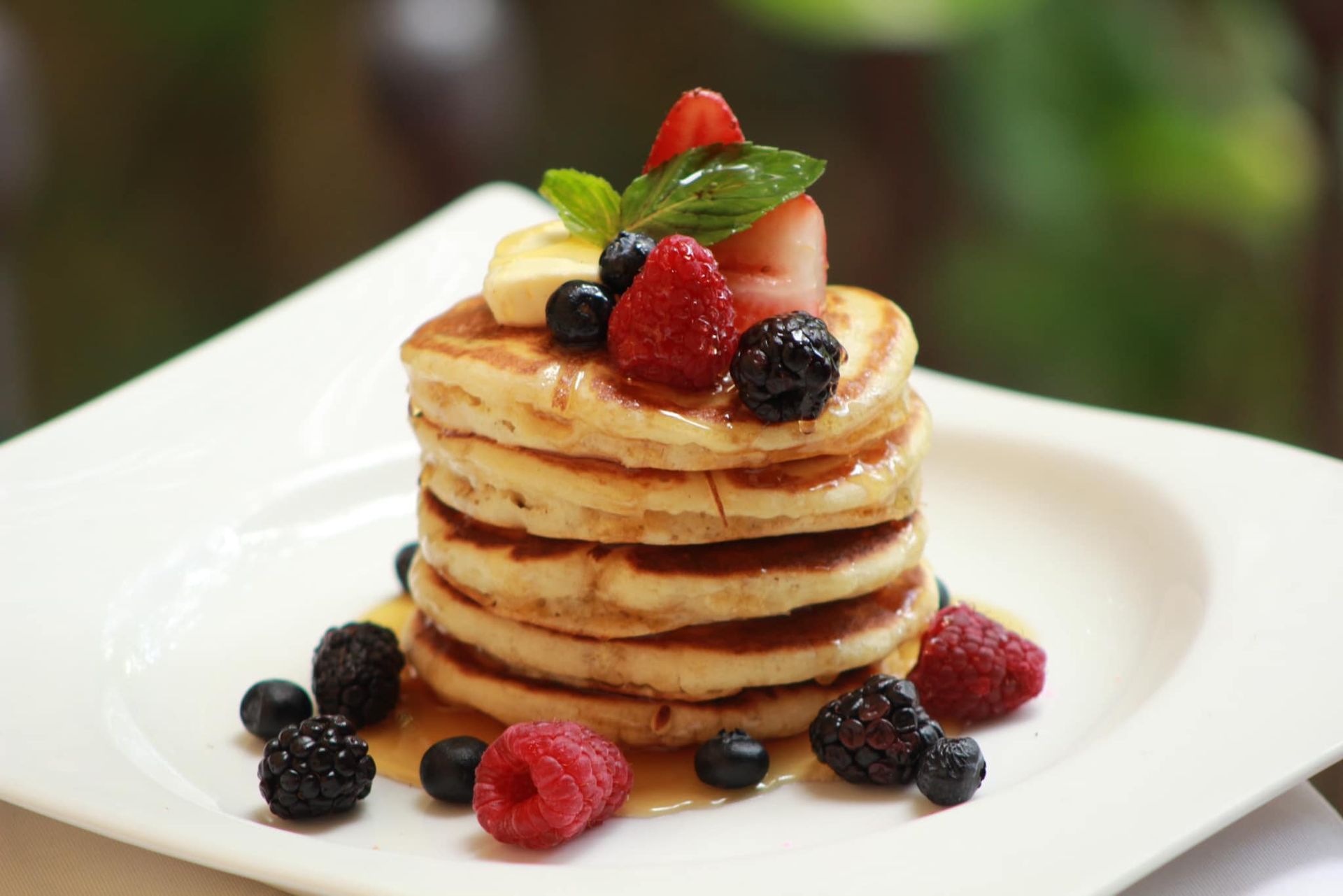 Pila de panqueques cubiertos con frutos rojos variados y jarabe en un plato blanco.