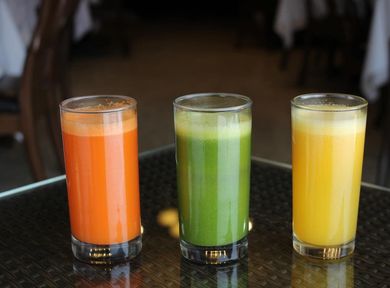 Tres vasos de jugo de naranja, verde y amarillo sobre una mesa.