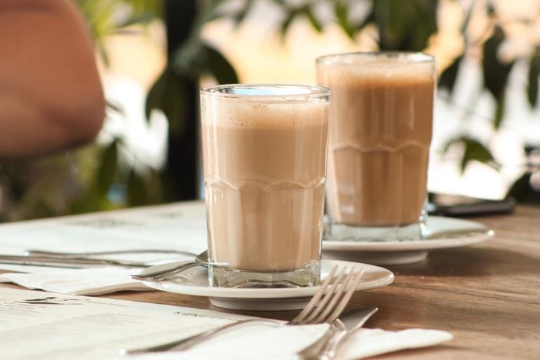 Dos vasos de café helado sobre una mesa de café iluminada por el sol, con platillos y cubiertos.