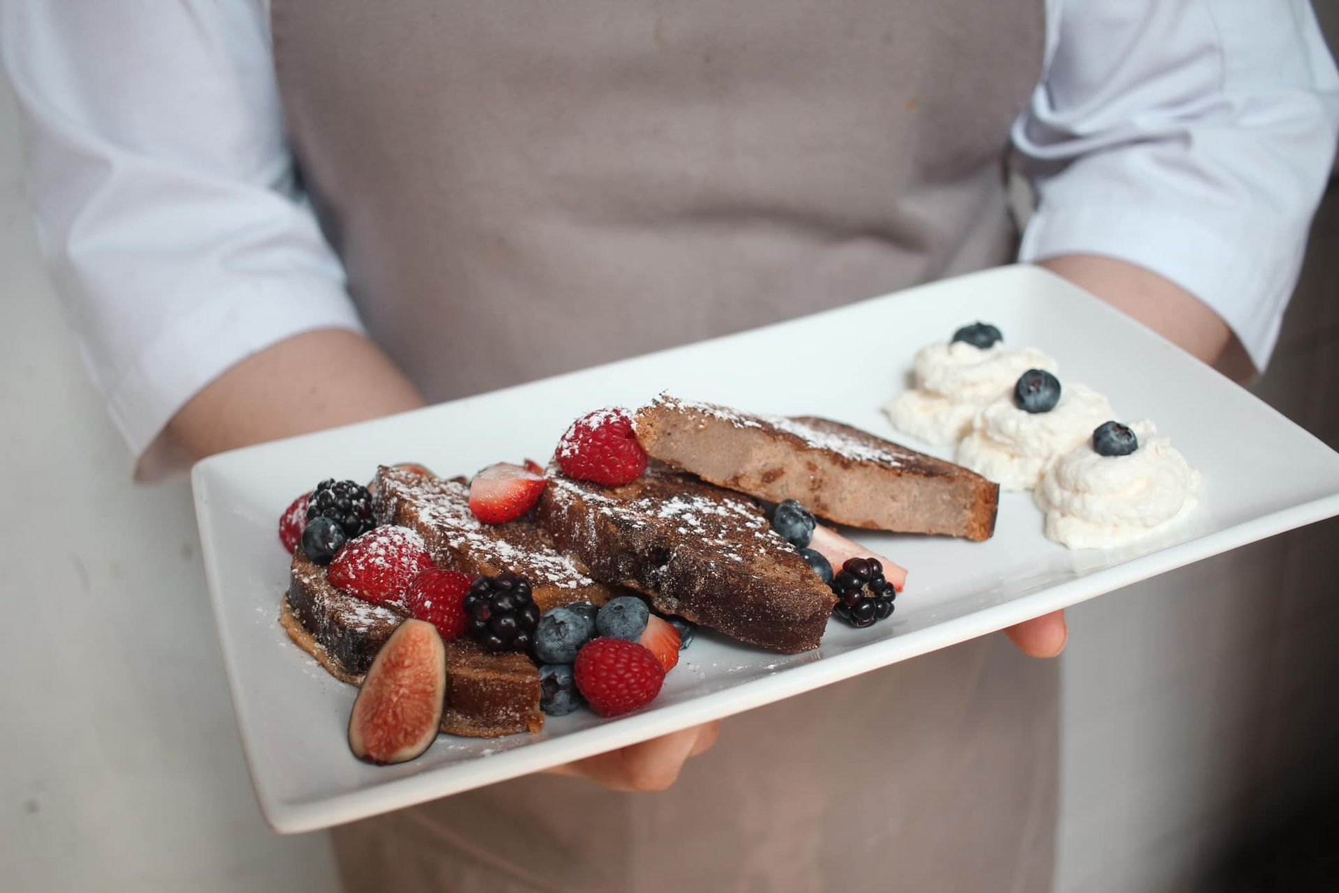 Persona sosteniendo una bandeja de postres de chocolate cubiertos con frutos rojos y crema.