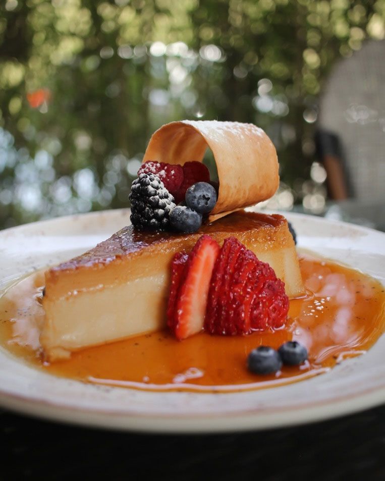 Postre de natillas con fresas, moras, arándanos y salsa de caramelo en un plato blanco.