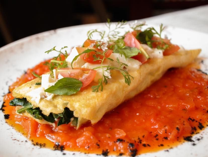 Crepe rellena de salsa roja, adornada con hierbas y verduras cortadas en rodajas finas.