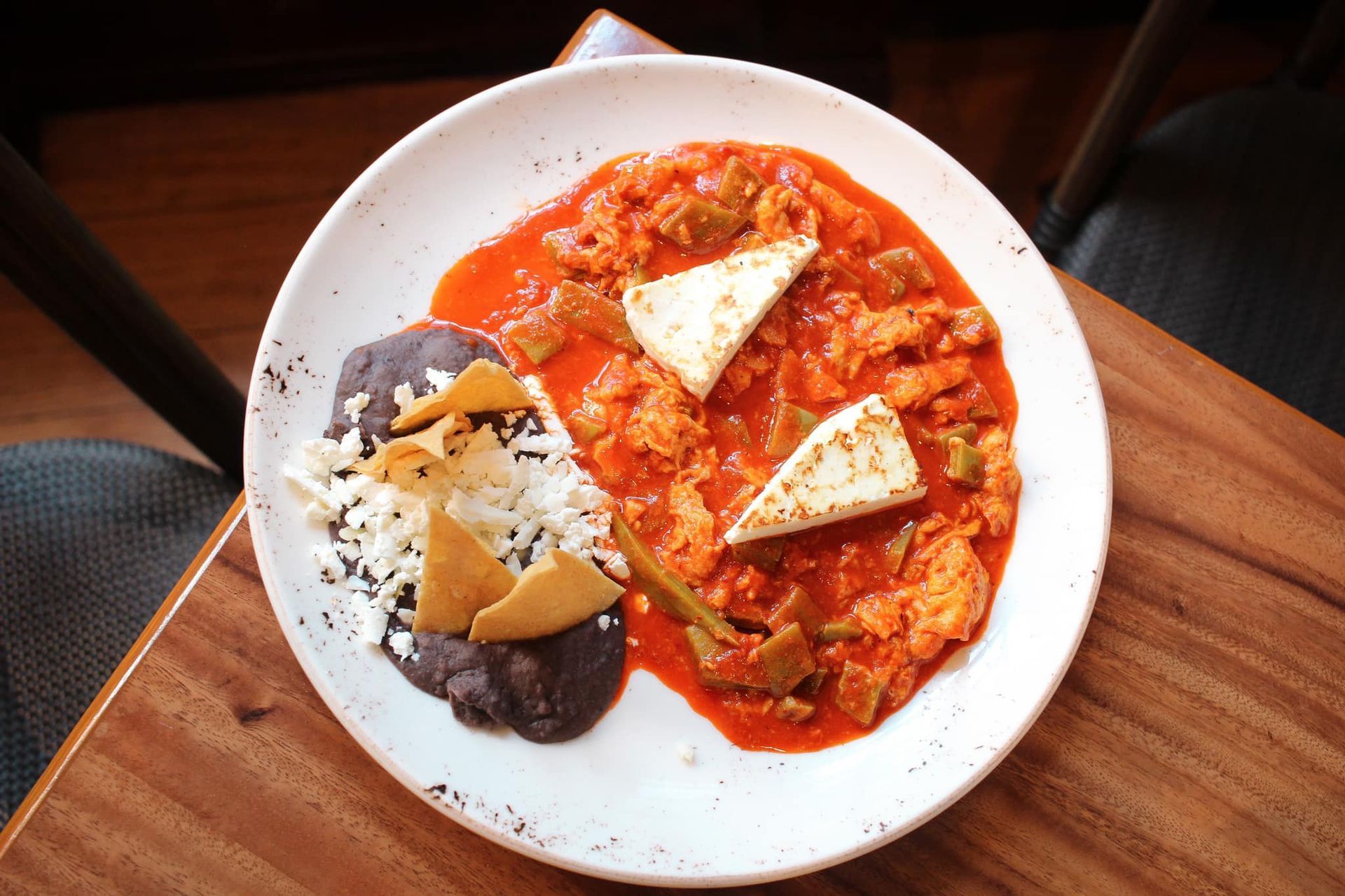 Plato de curry rojo con arroz, tofu y frijoles oscuros sobre una mesa de madera.