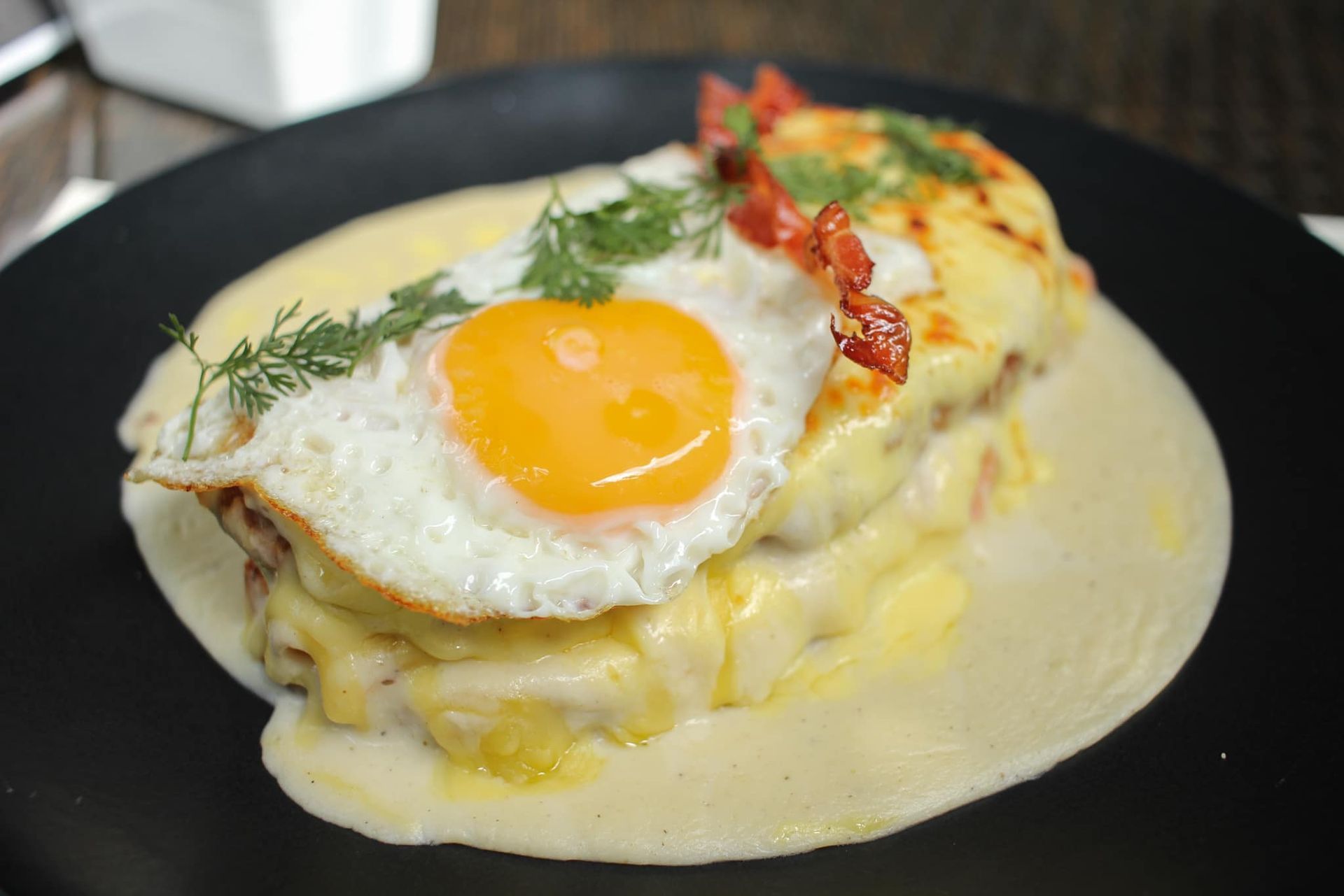 Tortilla cremosa con huevo frito y hierbas aromáticas sobre un plato negro.