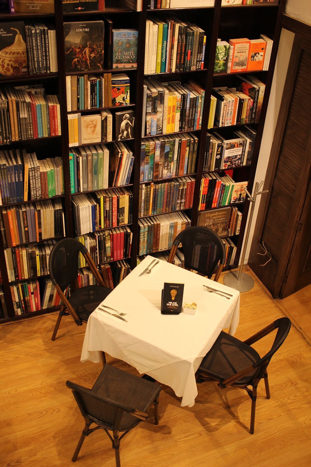 Mesita redonda con sillas en una acogedora librería, con estanterías llenas al fondo.