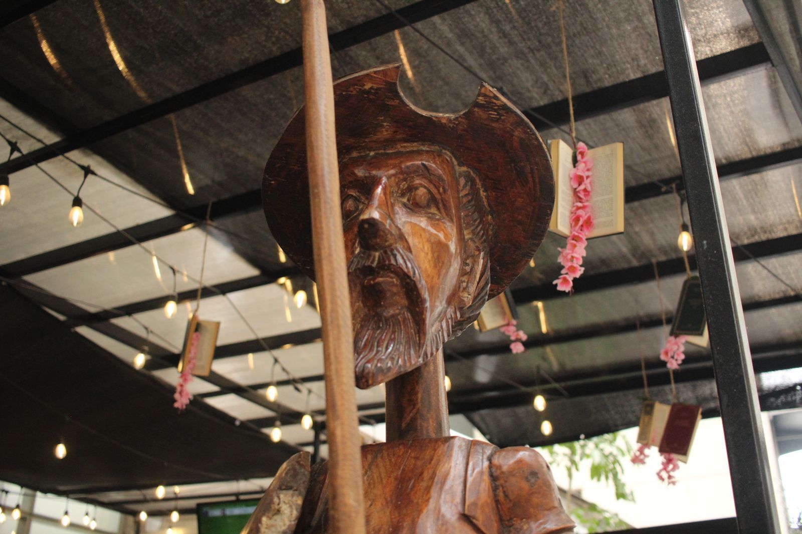 Estatua de madera de un vaquero bajo un techo de metal, sosteniendo un rifle y vistiendo un sombrero y un pañuelo rojo.