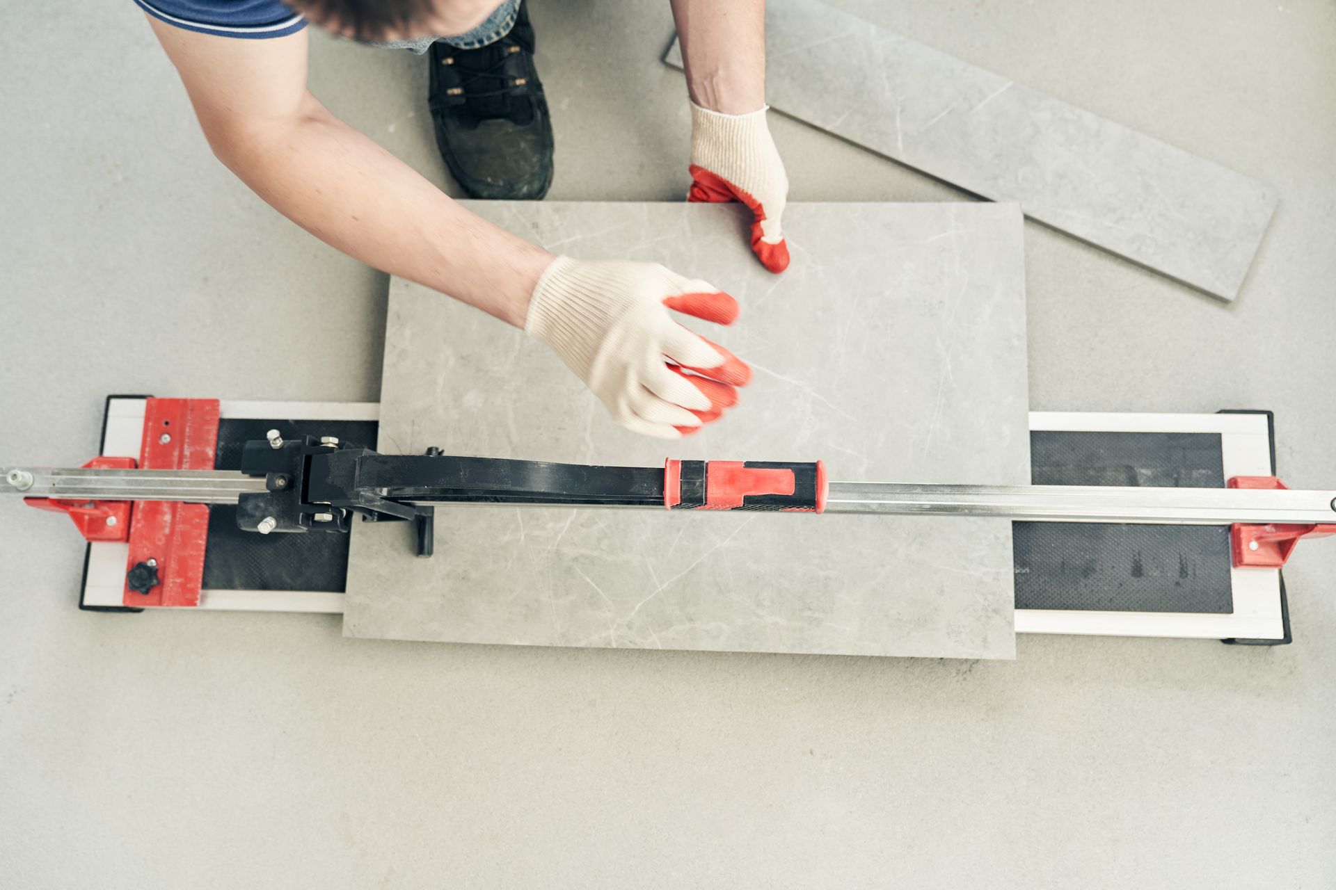 Hands in white gloves testing a gray tile with a clamp-style tool on a workbench