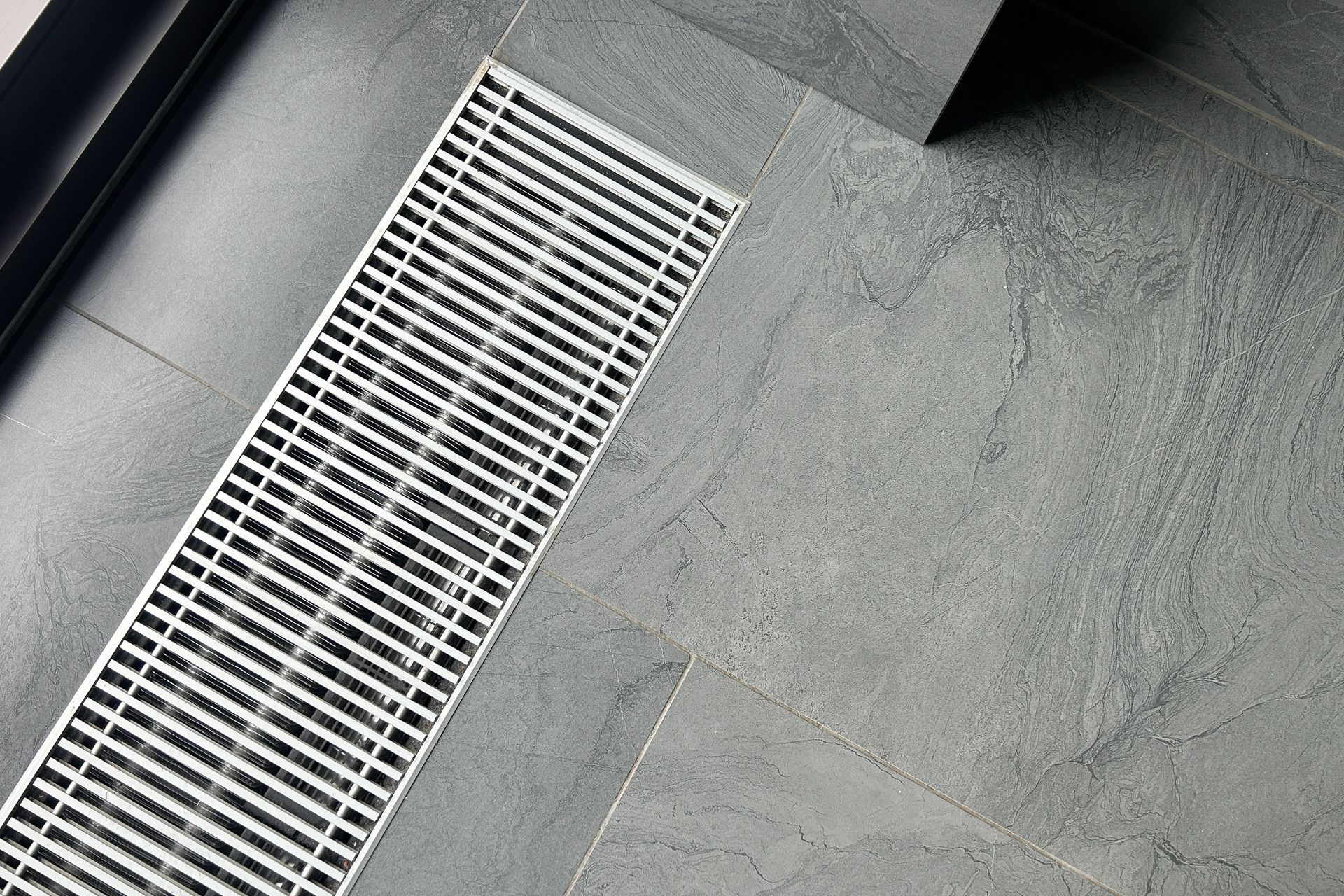 Gray tiled floor with a white metal floor drain grate