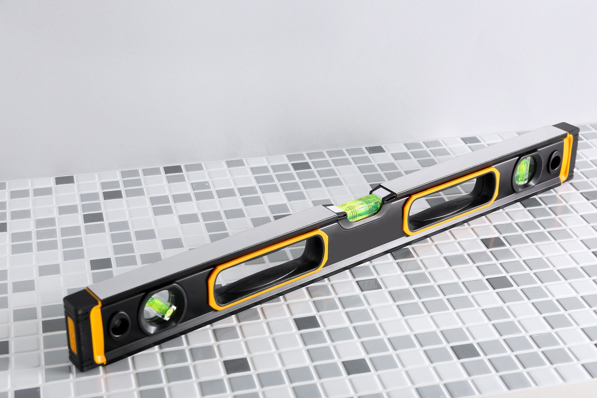 Black spirit level with green vials on a gray tiled surface