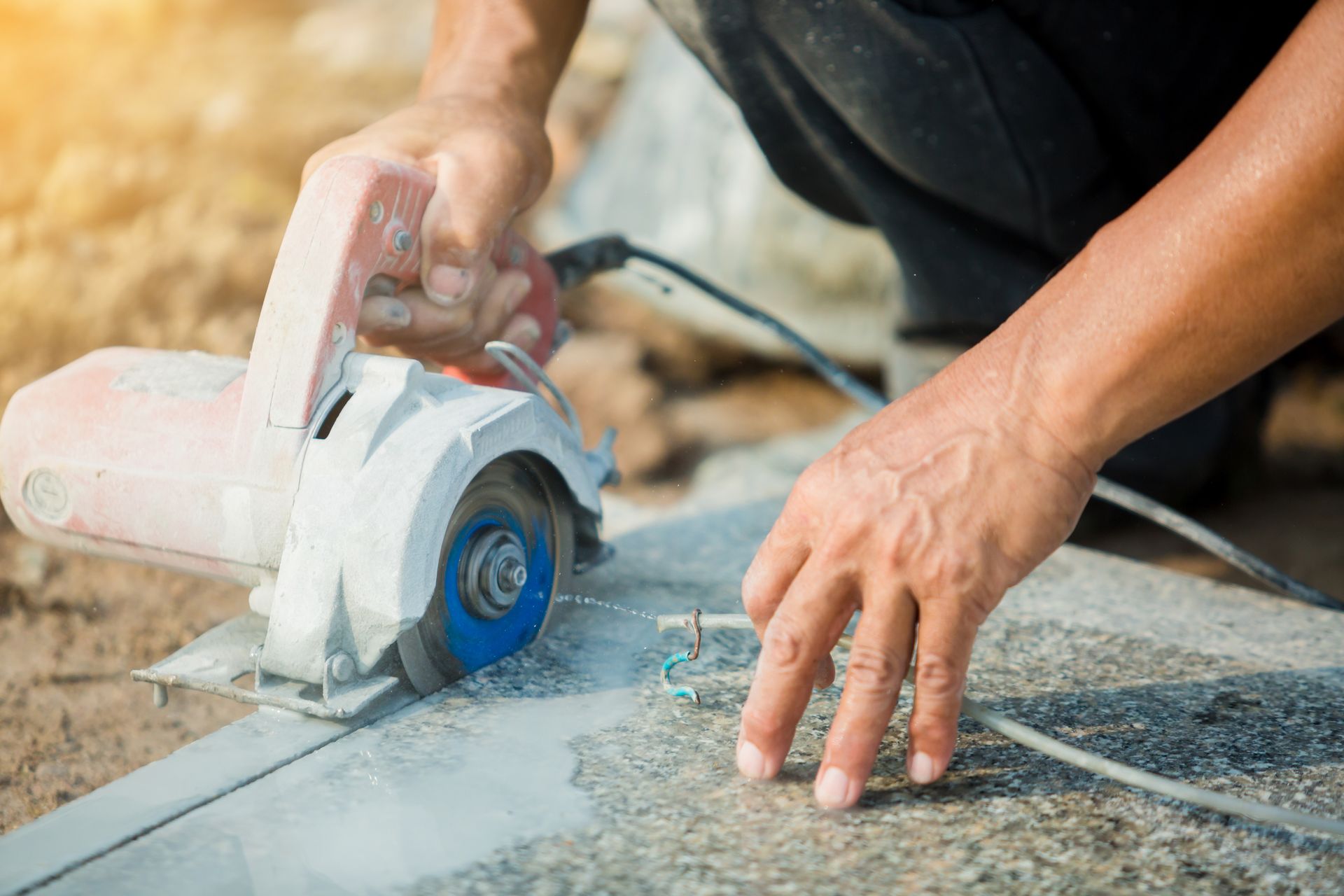 Hands using a circular saw to cut stone tile outdoors, with dust and debris visible