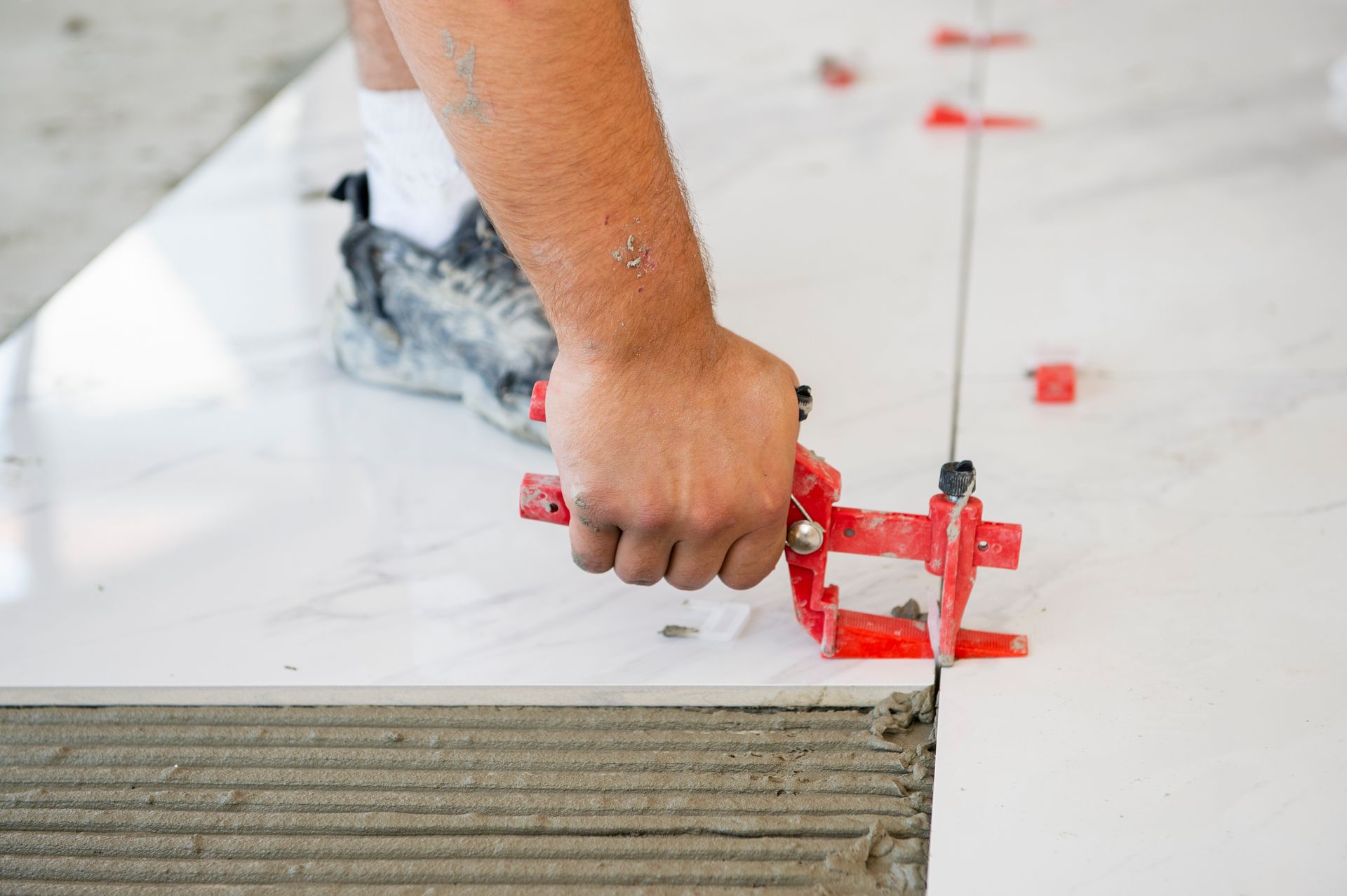 Hand placing a red tile-leveling tool on a white tile floor edge