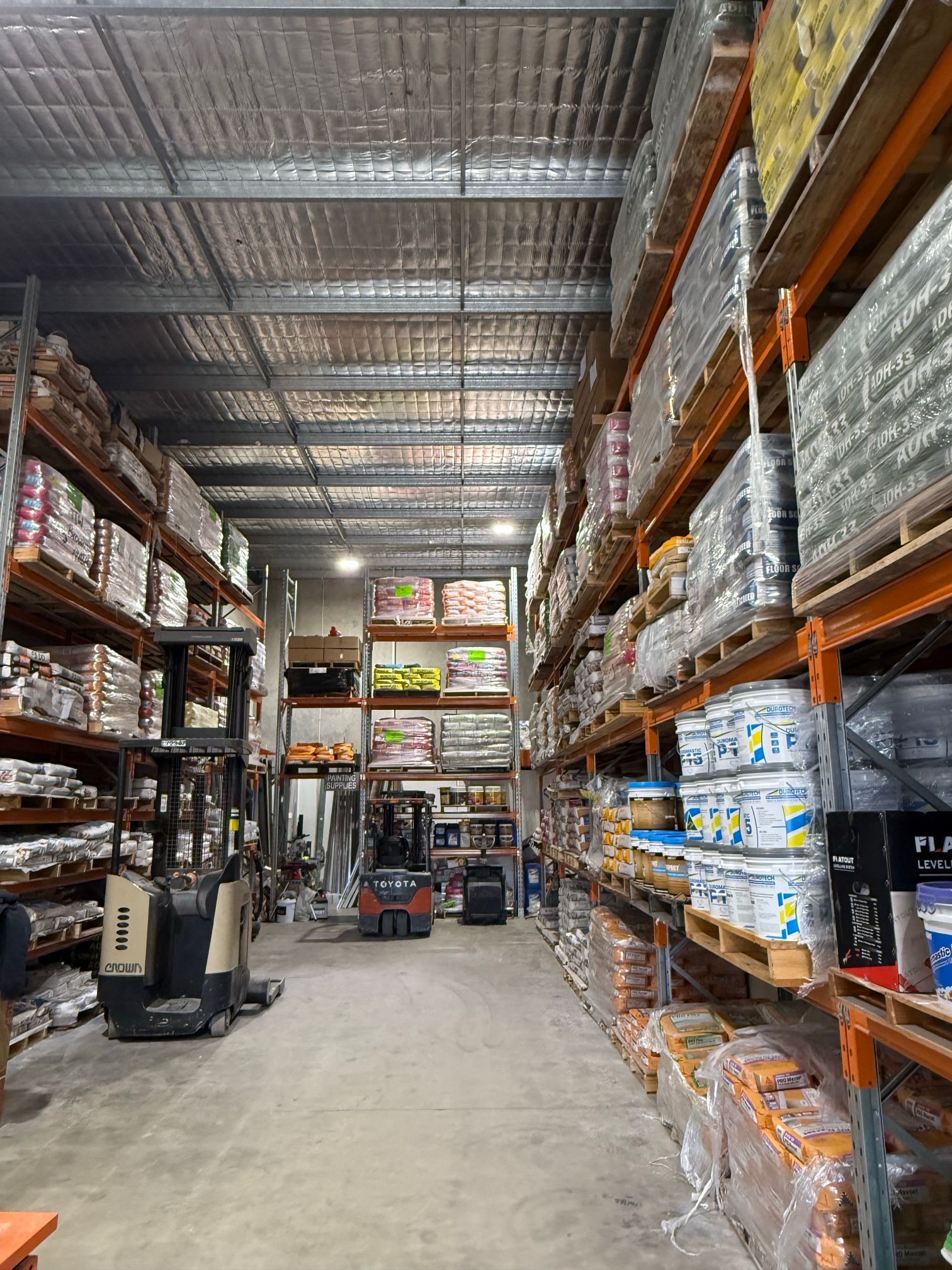 Aisle of a warehouse store with tall stocked shelves and a pallet jack on a concrete floor