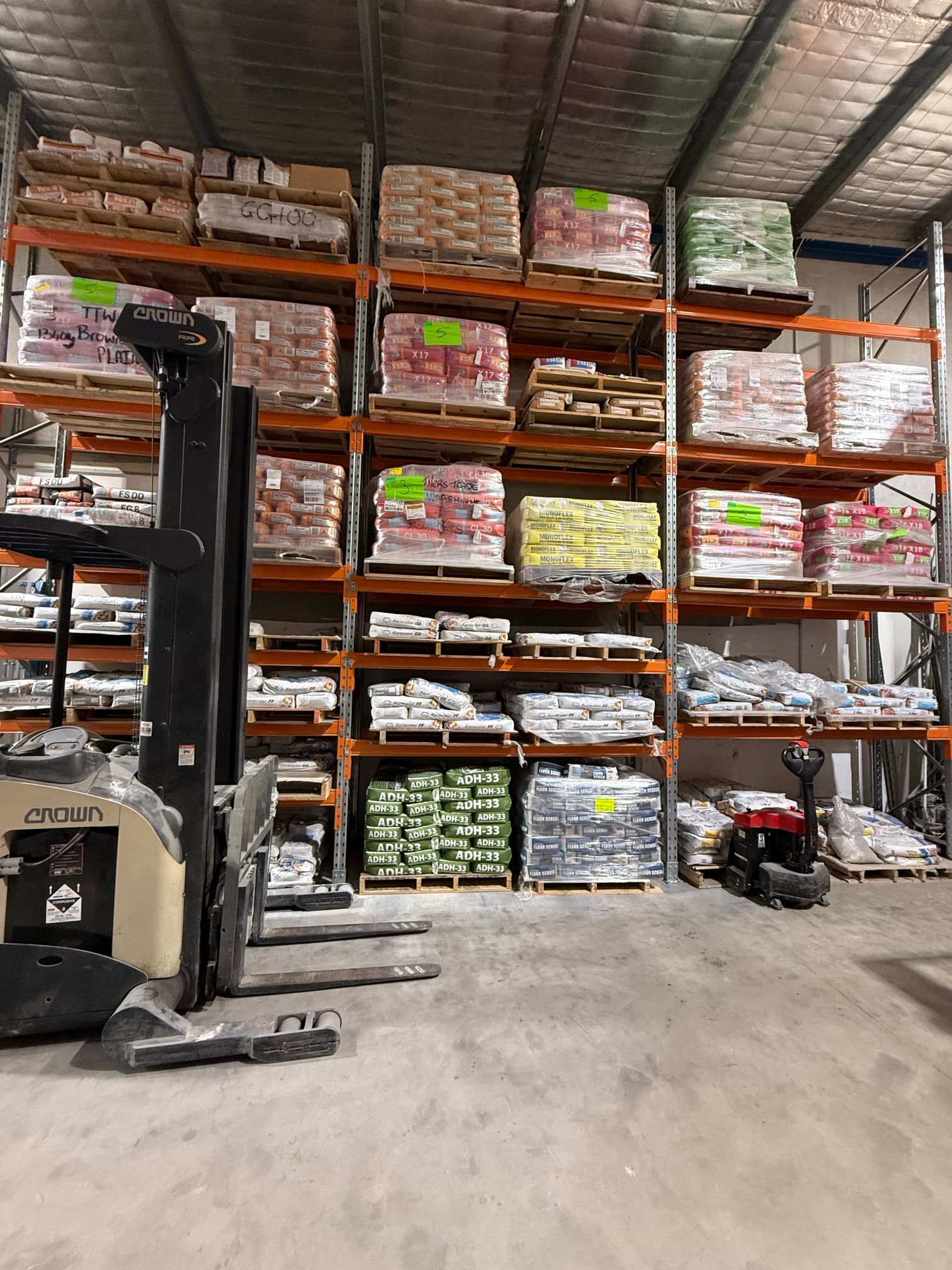 Warehouse aisle with stacked pallet racking, wrapped boxes, and a forklift in the foreground
