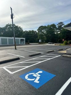 A freshly paved parking lot showing a blue and white accessible parking space symbol with adjacent hatched markings.