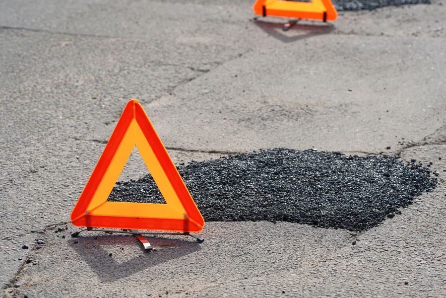 Two bright orange reflective warning triangles placed on a road next to fresh asphalt patches covering potholes.
