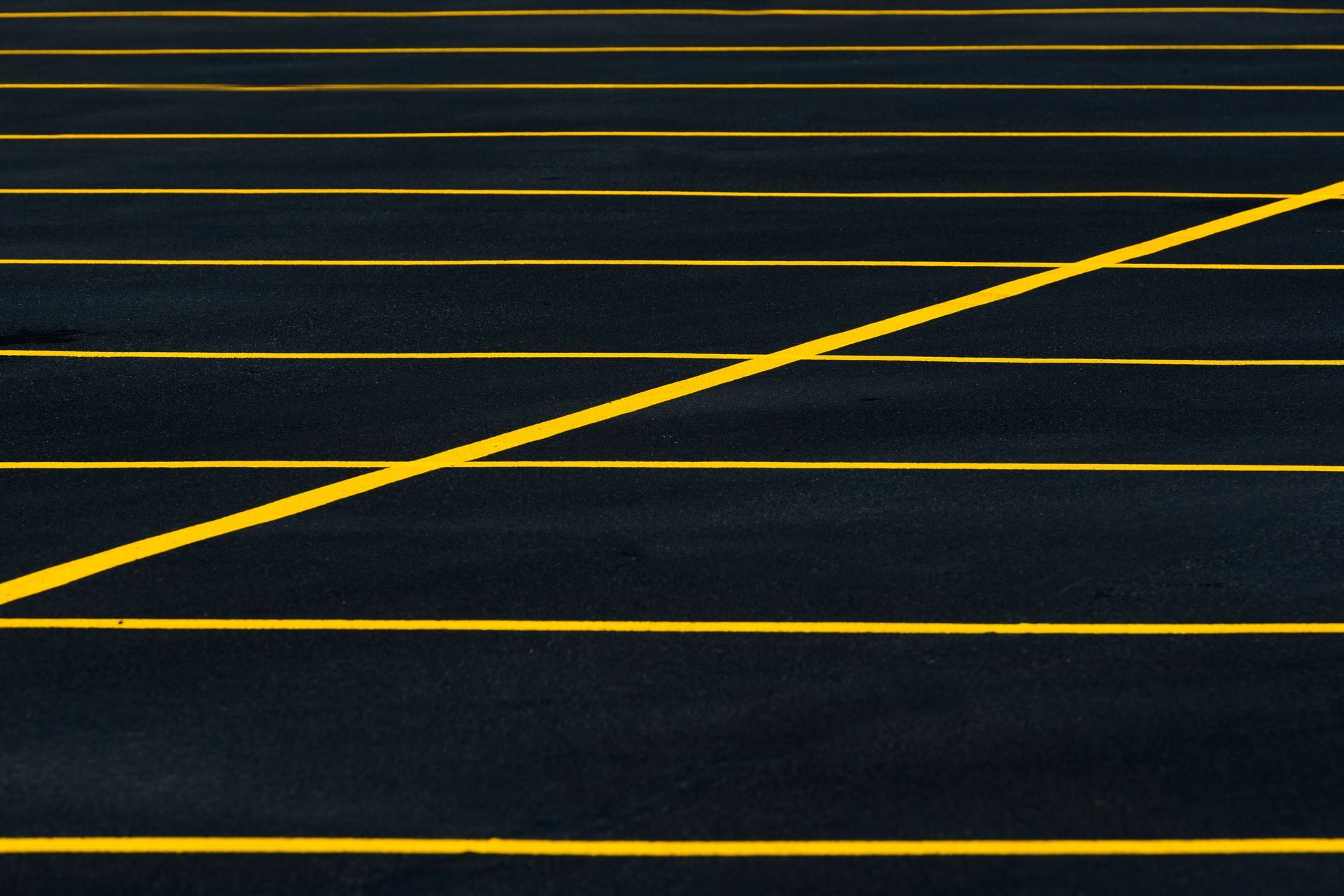 A diagonal yellow line crosses over several horizontal yellow lines painted on black asphalt.