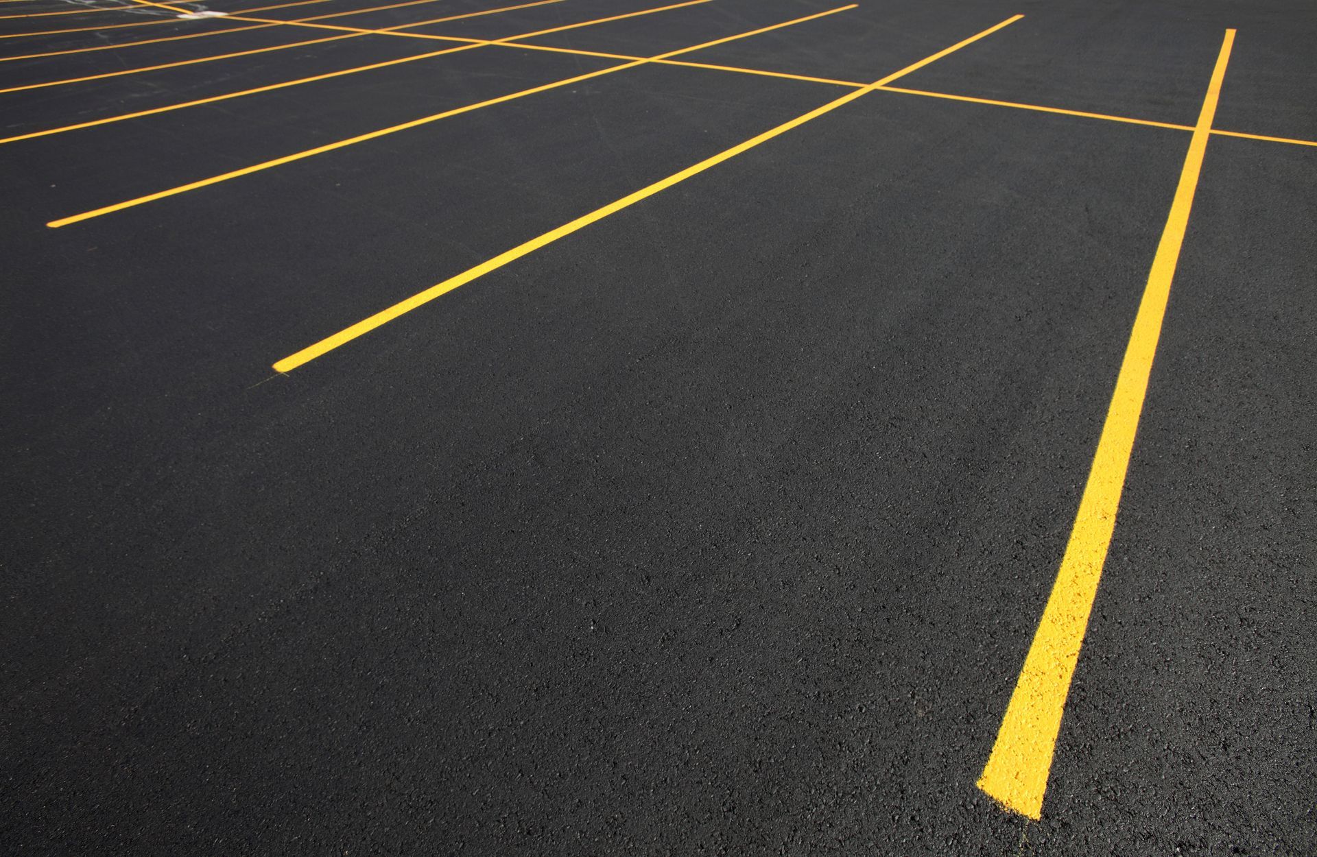An empty parking lot with bright yellow painted lines marking parking spaces on dark asphalt.
