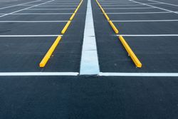 An empty parking lot with marked asphalt spaces, a central white dividing line, and yellow wheel stops.