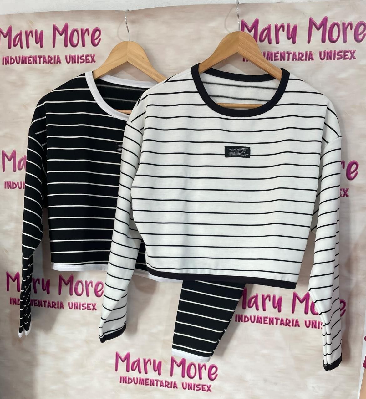 Dos camisas de rayas blancas y negras cuelgan en perchas frente a un cartel que dice Mary More.
