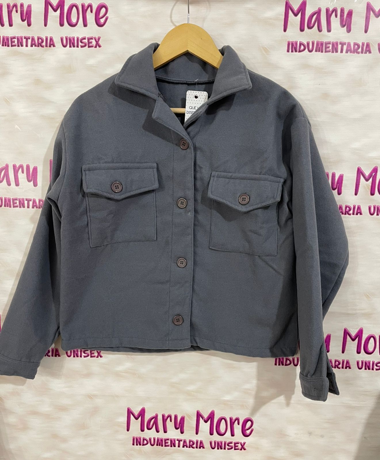 Una chaqueta gris está colgada en una percha delante de un cartel que dice maru more