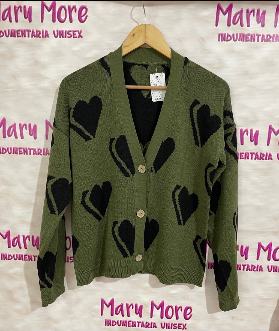 Un cárdigan verde con corazones negros cuelga de una percha.
