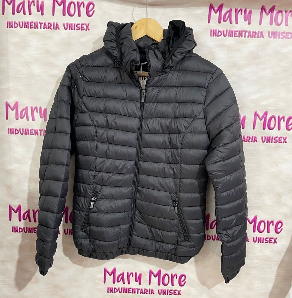Una chaqueta negra está colgada en una percha delante de un cartel que dice Mary More.