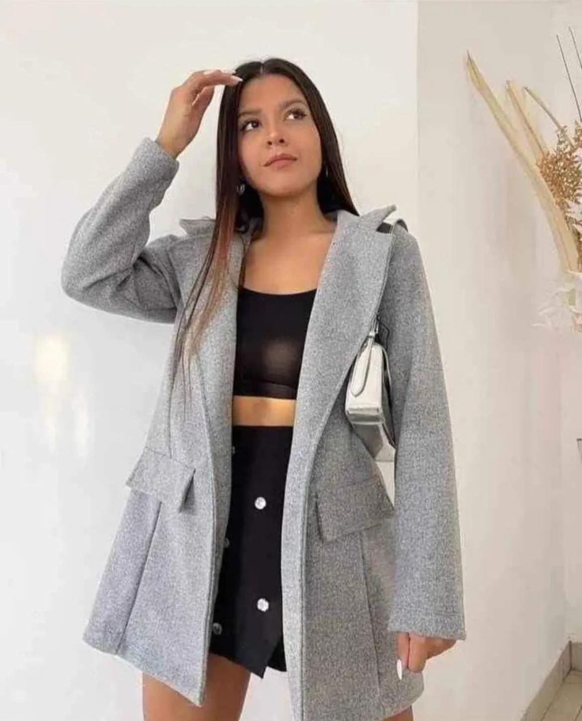 Una mujer lleva un abrigo gris y una falda negra.