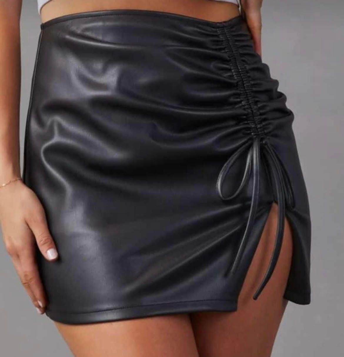 Una mujer lleva una falda de cuero negra y un top corto blanco.