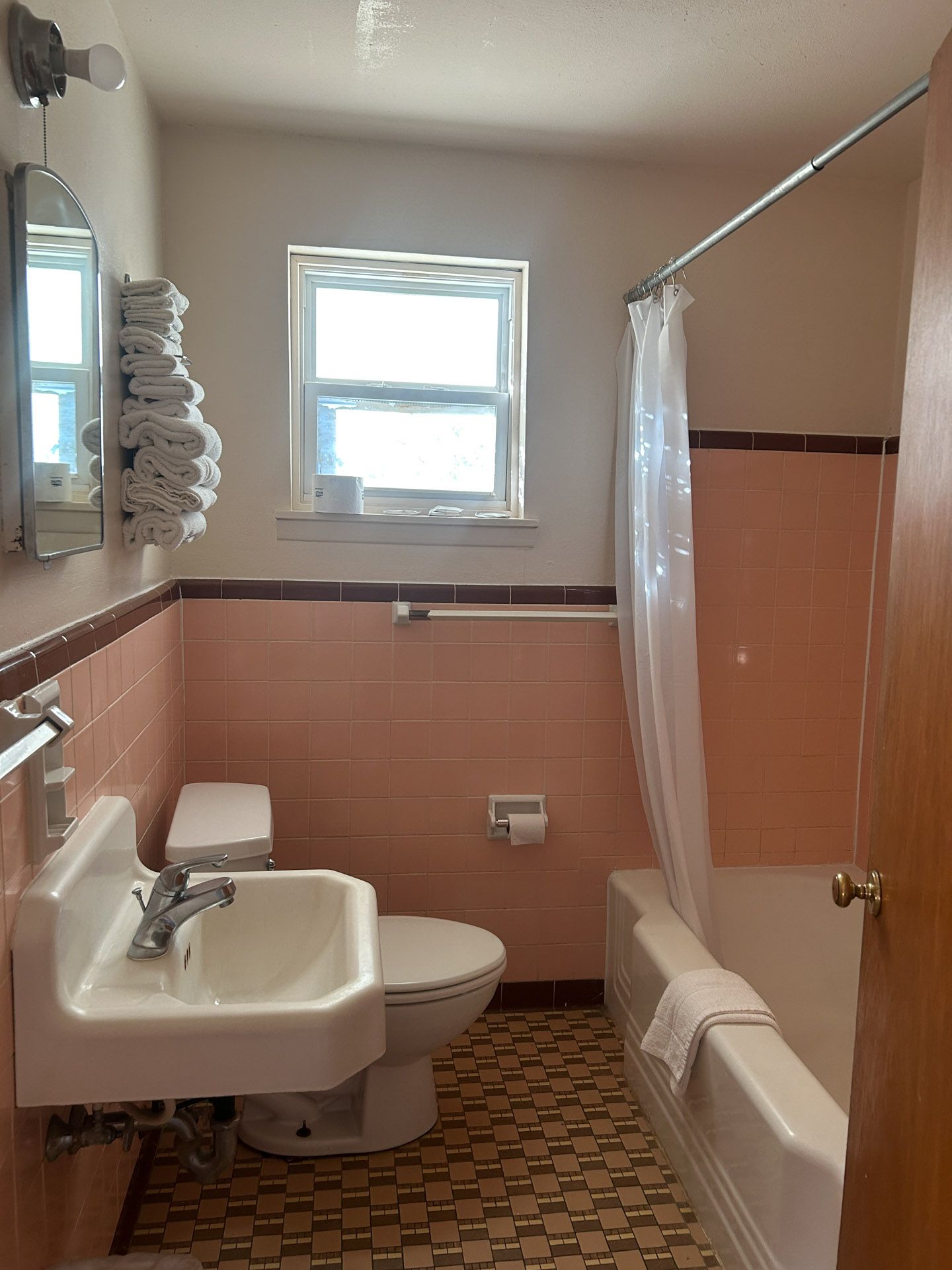 Pink-tiled bathroom with a sink, toilet, tub, and window. A shower curtain hangs.