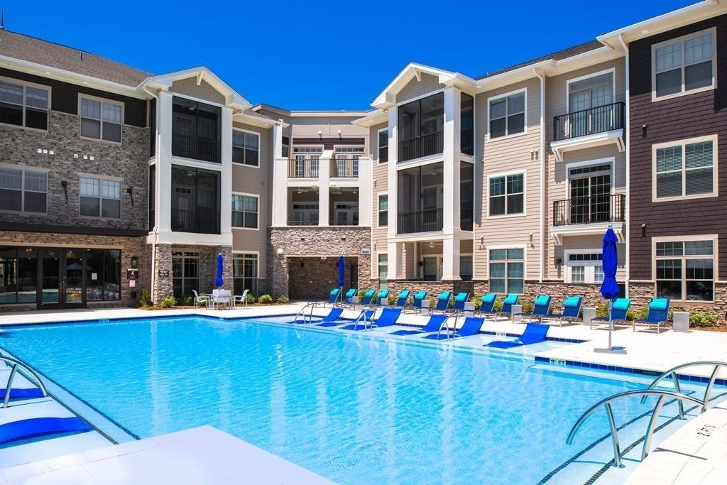 A bright blue swimming pool sits in front of a multi-story apartment complex with stone and tan siding on a sunny day at Silver Collection at the Park..