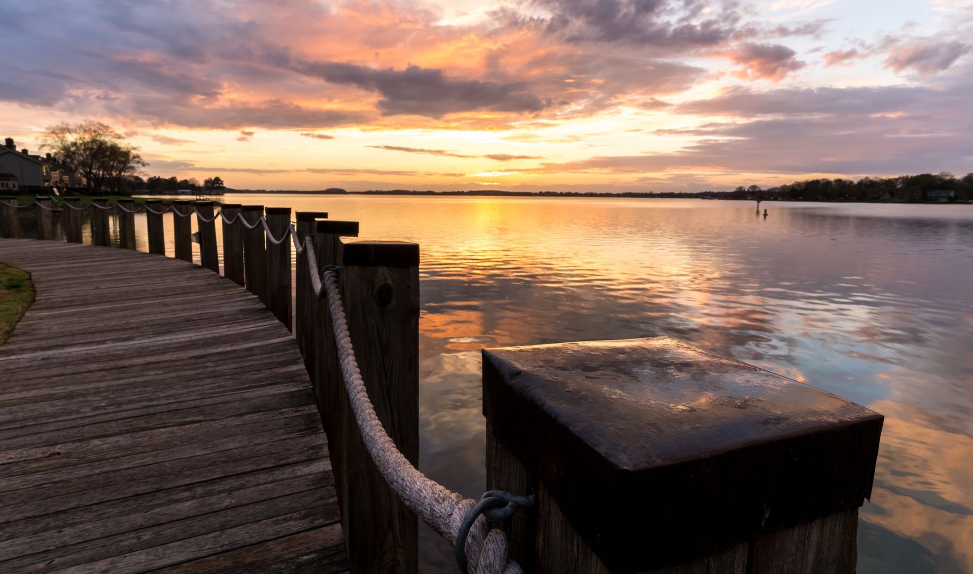 Wooden boardwalk leading to a calm lake reflecting a vibrant sunset with orange and purple hues at Silver Collection at the Park.