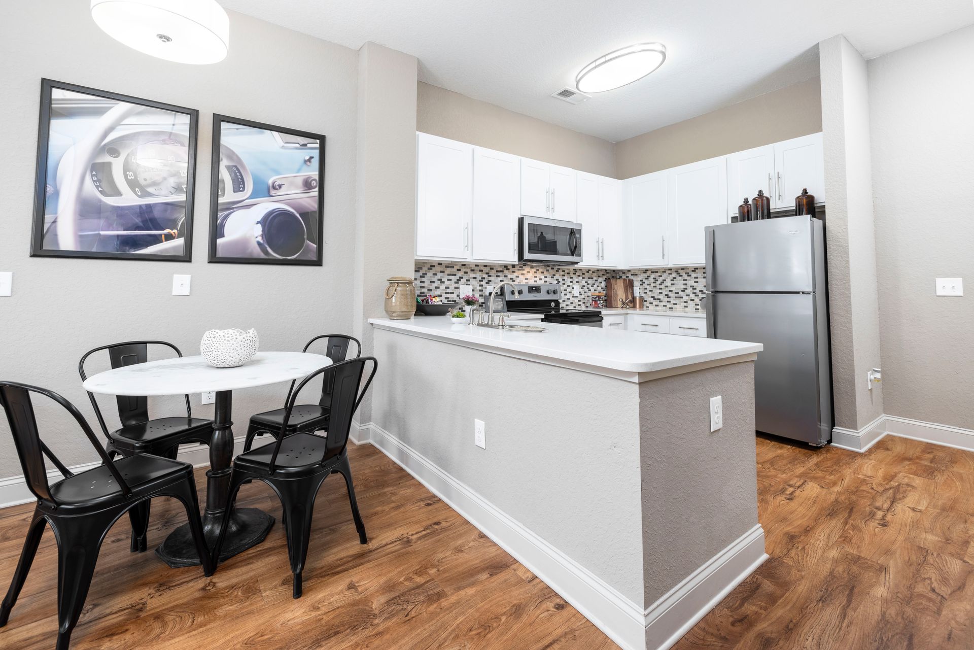Modern kitchen featuring white cabinets, stainless steel appliances, and a small dining table with four black chairs.