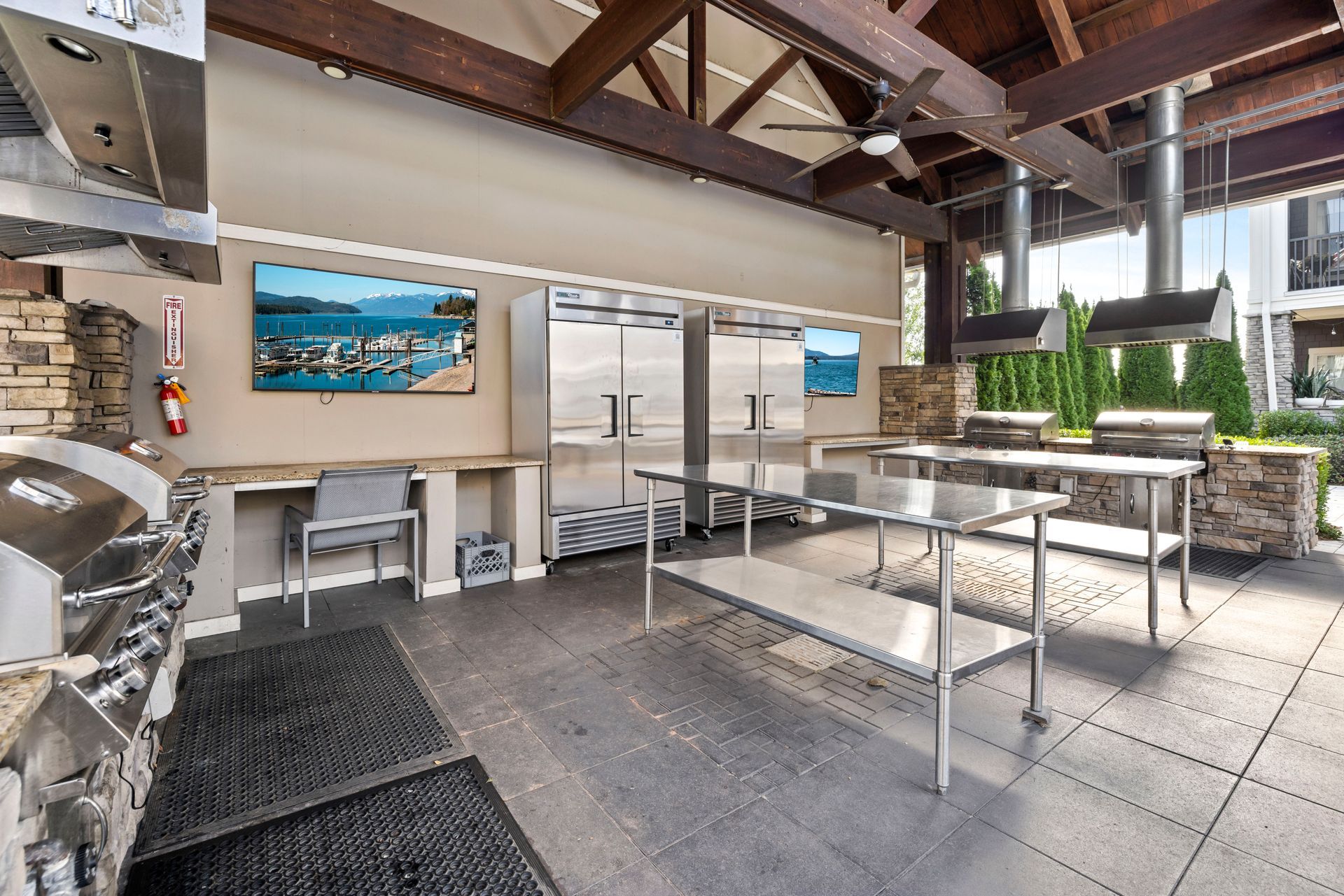 An outdoor commercial kitchen featuring stainless steel grills, prep tables, refrigerators, and a mounted flat-screen TV at Silver Collection at the Park..
