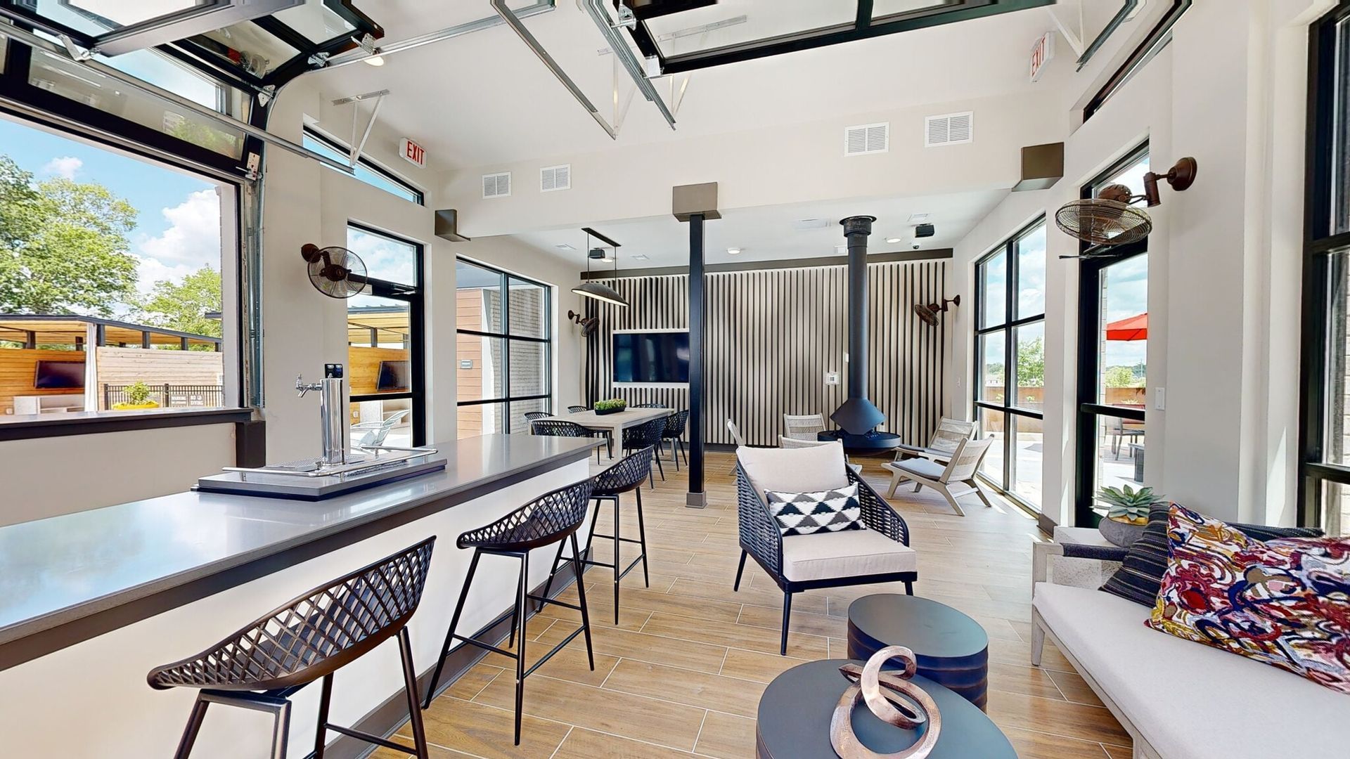 Spacious indoor community lounge with a bar, stools, seating area, and large windows.