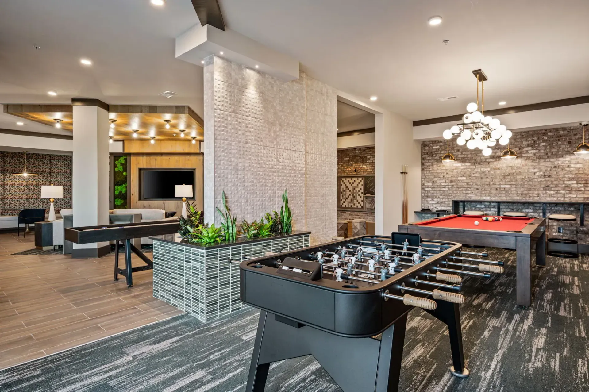 Indoor community lounge with foosball and pool tables, seating, and a wall-mounted TV.