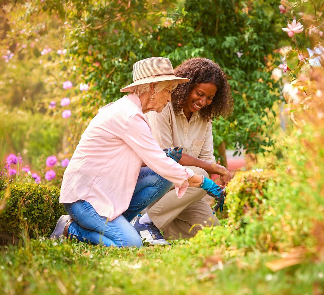 Smiling caregiver walking outdoors with happy elderly female resident at Brookside Commons wooded campus