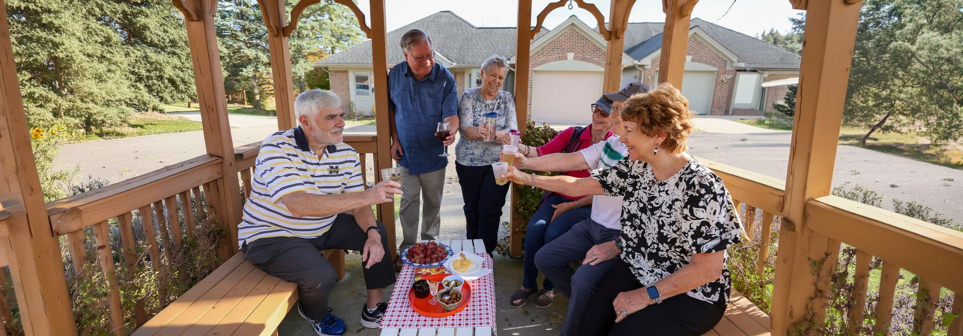 Five people seated on a wooden gazebo porch sharing a picnic with drinks and fruit table centerpiece