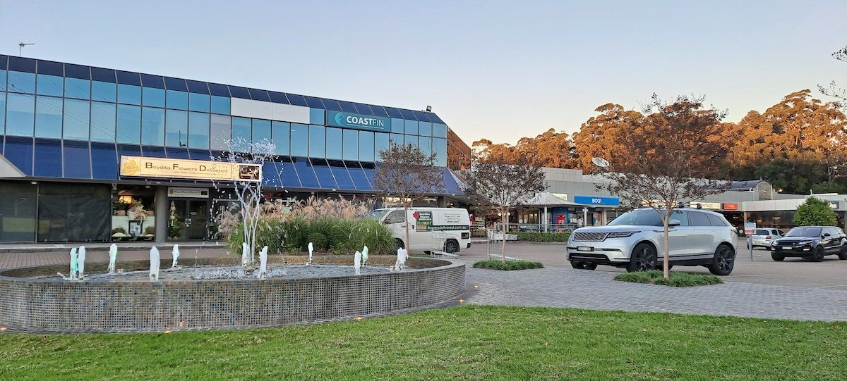 A Car Is Parked In Front Of A Building Next To A Fountain — BAS Plumbing & Drainage In Erina, NSW