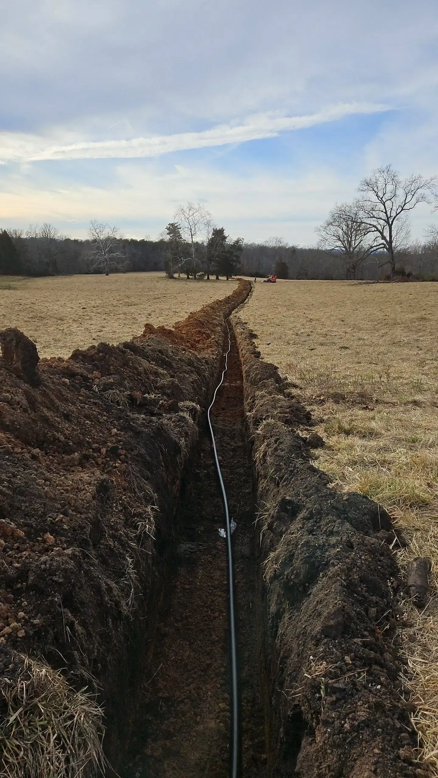 A trench in the middle of a field with trees in the background.