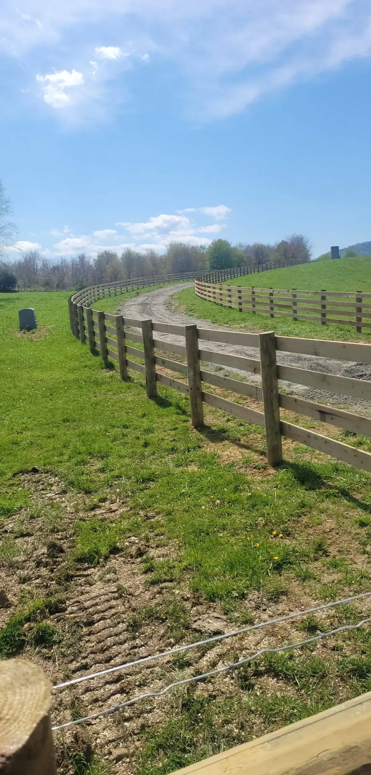 A wooden fence surrounds a grassy field on a sunny day.
