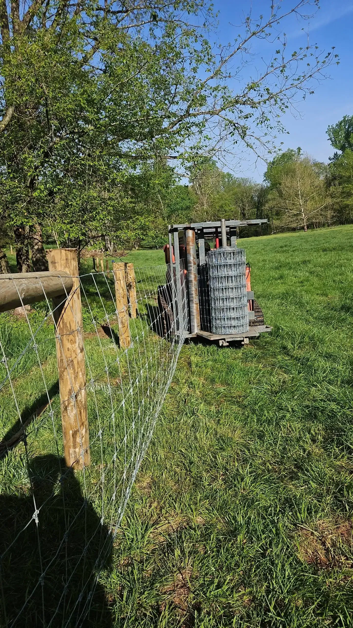 A tractor is parked in a grassy field next to a wooden fence.