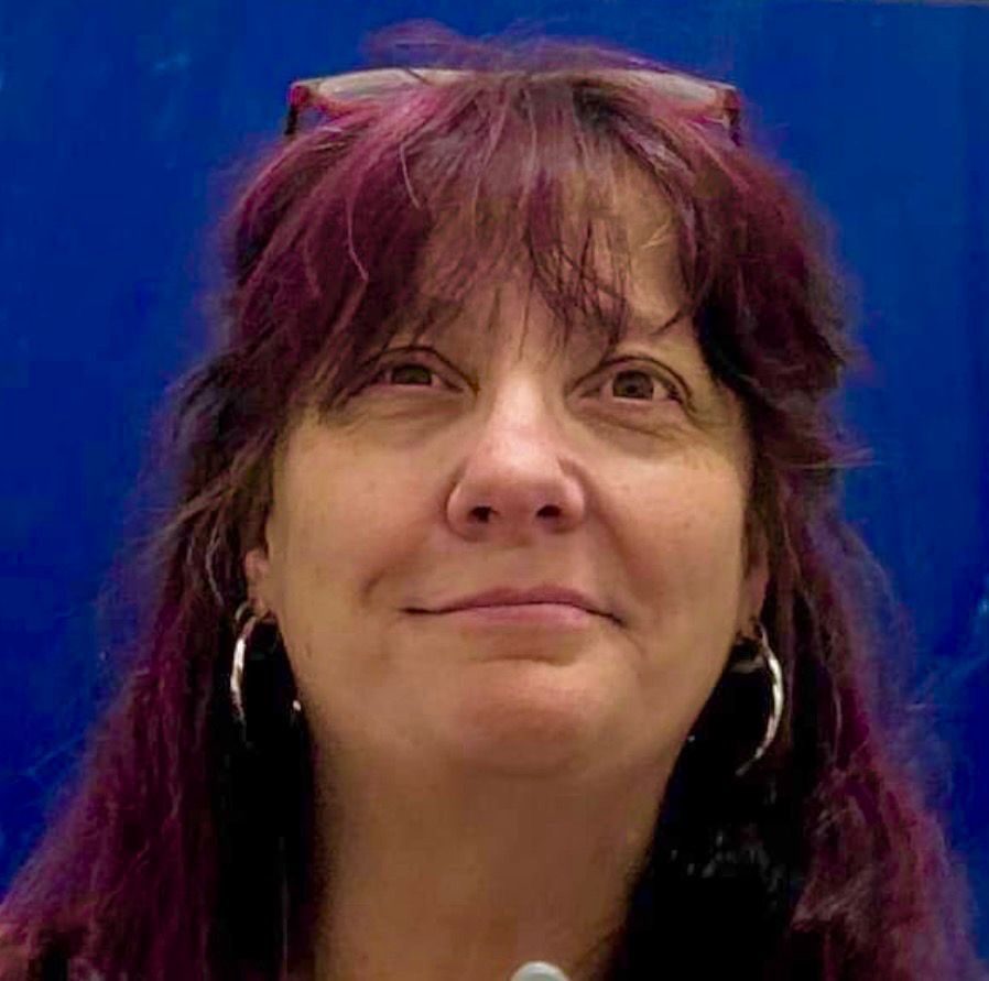 A woman wearing glasses and earbuds is smiling for the camera.