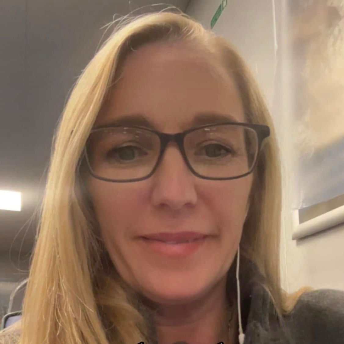 A woman wearing glasses and earbuds is smiling for the camera.